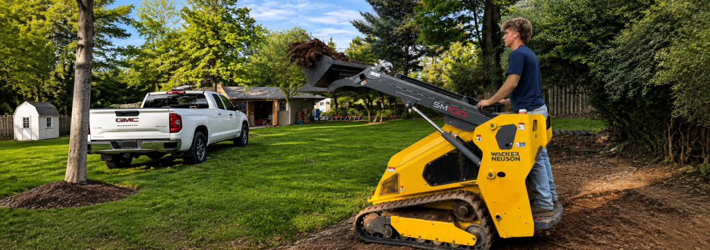 Land Clearing Cost Estimate Factors | Yellow Wacker Neuson skid steer loader clearing brush and debris from a suburban residential lawn